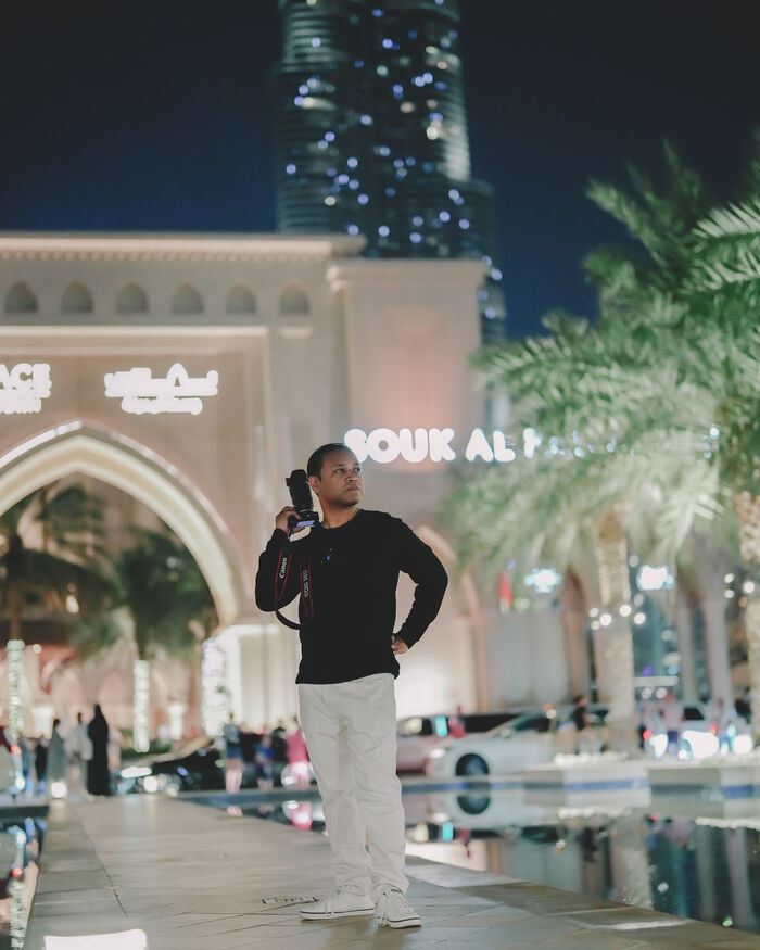 A man with a camera over his shoulder, standing outside a lit souk at night